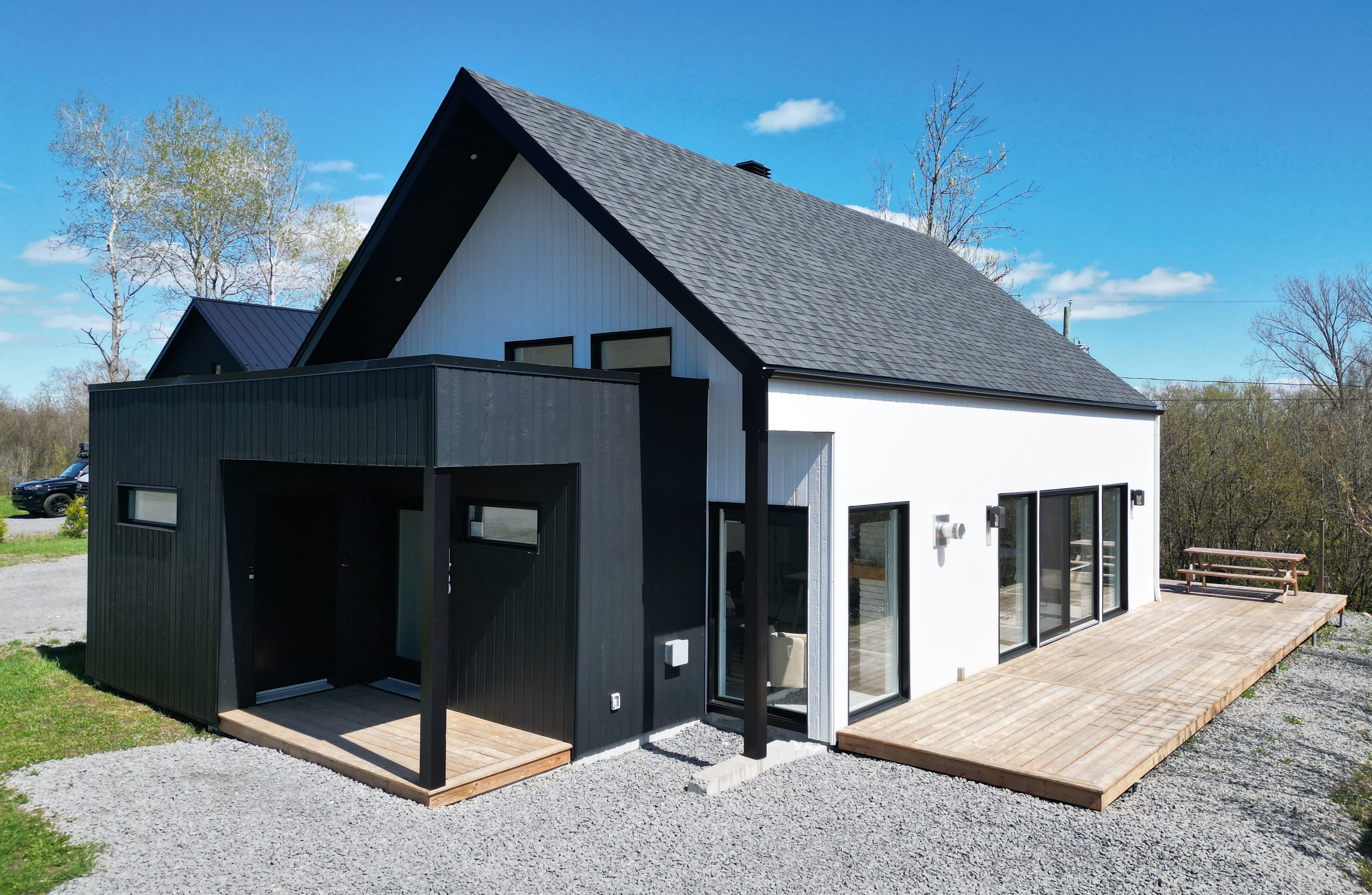 Chalet contemporain Monsieur Ferréol à Saint-Ferréol-les-Neiges : façade noire et blanche, terrasse de bois et ciel bleu